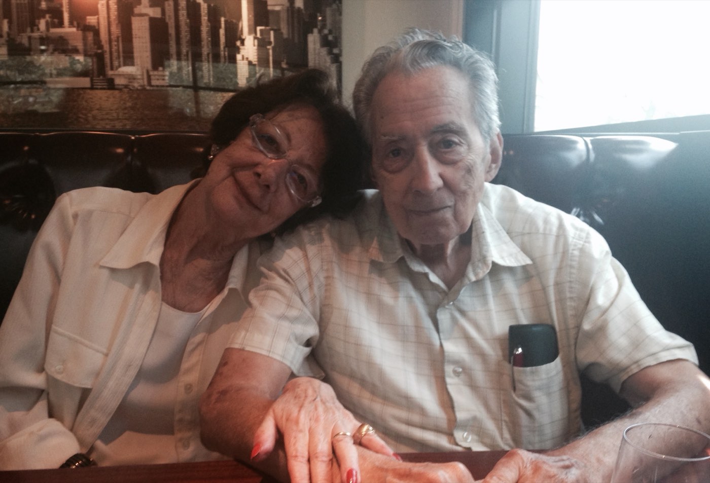 Anne Polajenko resting her head on Nicholas Polajenko's shoulder in a restaurant booth, their hands together on the table, May 2015