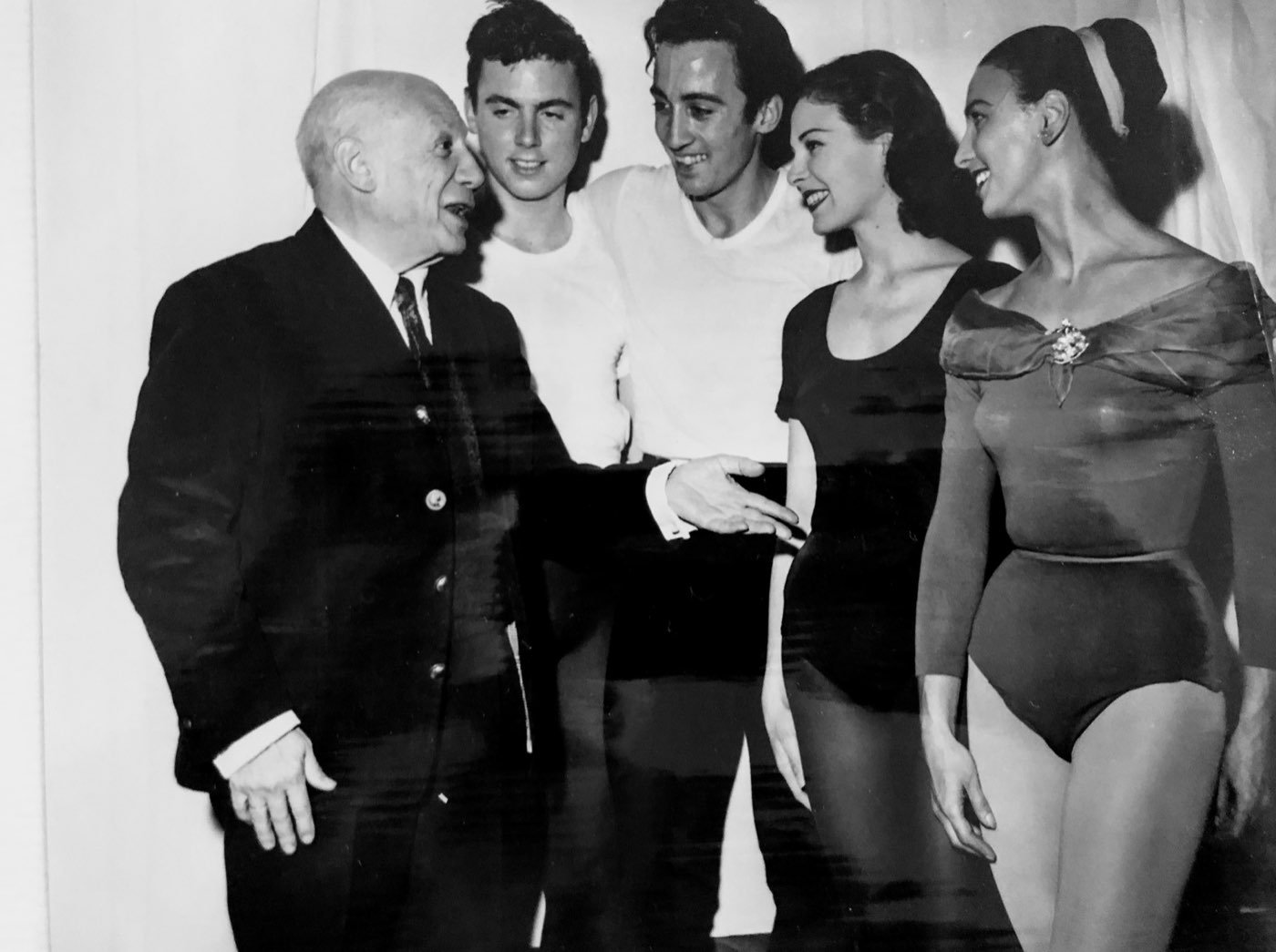 Pablo Picasso, in a dark suit, talking and laughing with four young dancers in rehearsal clothes; Nicholas Polajenko stands third from left in a white shirt